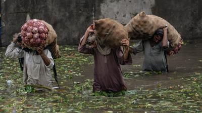 Labourer carries a basket loaded with vegetables in a flooded area 
