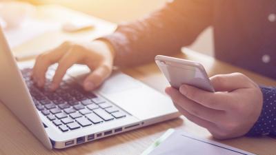 A generic photo of someone working at a desk with a laptop and mobile phone.
