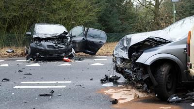 A photograph of a road traffic accident. Two cars can be seen smashed and broken on a tarmac road.