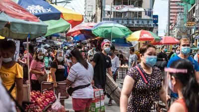 A photograph of a busy street market in Asia, with people moving and selling goods seen wearing face masks.