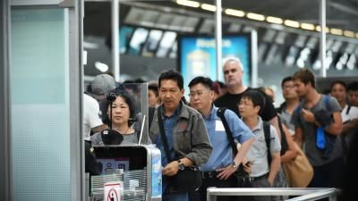 People queuing in an airport at passport control. People can be seen holding bags, standing in line.
