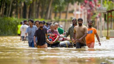 A group of men helping two elderly people during a flood. The elderly couple can be seen in a dinghy of a flooded street with six men pulling it.