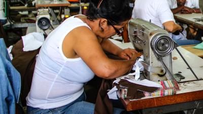 A photograph of a woman using a sewing machine in a garment factory.