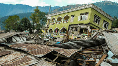 The aftermath of an earthquake in Pakistan, a building has been toppled and rubble can be seen everywhere.