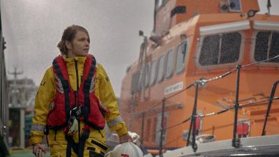 An Royal National Lifeboat Institute crew member standing in the rain by an RNLI ship.
