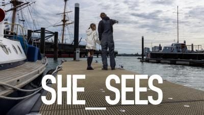 A photograph of a young girl and man pointing at boats in a harbour.