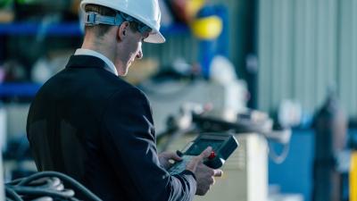 Business professional in safety helmet using handheld device in industrial workplace 