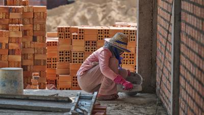 construction worker is crouched over, building brick wall 