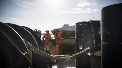 Two workers in bright orange safety gear on a vessel deck with industrial equipment.