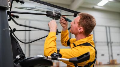 Technician in yellow uniform using a screwdriver to repair vehicle