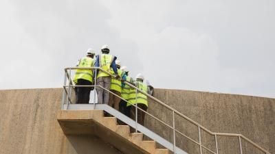 Construction workers in high-visibility vests and hard hats ascending concrete stairs at a worksite.