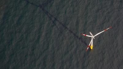 Aerial view of an offshore wind turbine with red-tipped blades standing in dark water.