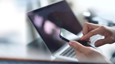 Hands using smartphone next to laptop