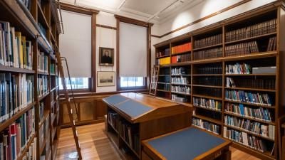 Traditional library reading room with wooden bookshelves, sliding ladders, and reading tables with blue surfaces.