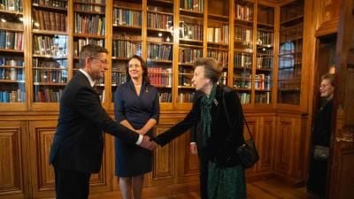 A formal meeting in an elegant library with wooden bookshelves, where people are greeting each other with a handshake.