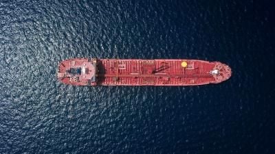 Aerial view of a large red oil tanker ship sailing across deep blue ocean waters.