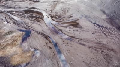 Aerial view of a marshy landscape with flowing water patterns and muddy terrain in muted colors.