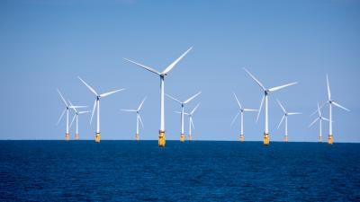 Offshore wind farm with multiple white turbines rising from deep blue ocean under clear sky.