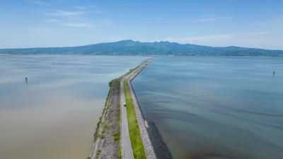 Aerial view of a narrow causeway stretching across a lake with mountains in the background.