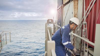Worker in blue coveralls and white helmet performing maintenance on offshore platform at sea.