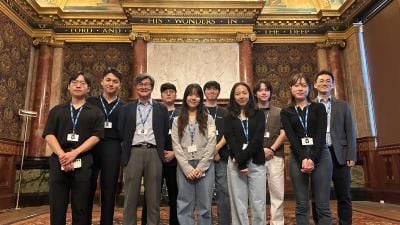 A group of attendees wearing ID badges standing in an ornate hall with "LORD" and "WONDERS IN THE DEEP" inscribed above.