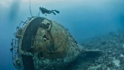 Scuba diver exploring a sunken submarine wreck in deep blue waters.