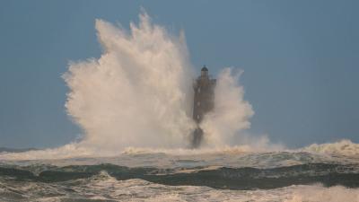 Lighthouse standing amid powerful ocean waves, with water dramatically crashing against it.