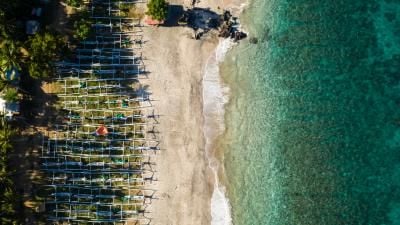 Aerial view of beach with fishing boats lined up on the shore beside turquoise waters.