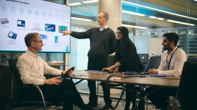 Business meeting with presentation showing "Navigating the transition" timeline from 2015-2025 with digital transformation milestones.