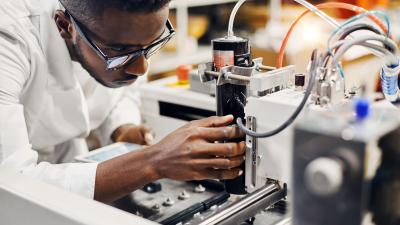 engineer in lab coat carefully adjusting laboratory equipment with tubes and wires connected to a testing apparatus.