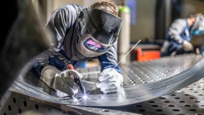 Welder in protective gear working on metal sheet with welding torch in workshop.