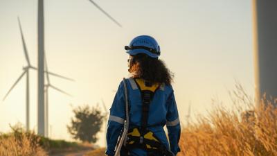 female in blue safety gear looking at wind turbines during sunset.