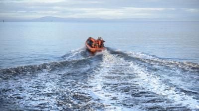 Small orange rescue boat speeding across calm sea, creating wake patterns with distant mountains visible.
