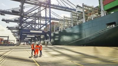 Port workers in safety gear observing massive container ship being loaded by large cranes.