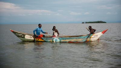 Three fishermen in a colorful wooden boat on a lake, with a small island visible in the distance under cloudy skies.