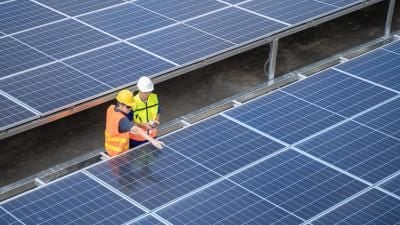 Two workers in safety gear inspecting solar panel installation on a large array.