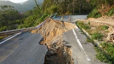 Collapsed mountain road with severe landslide damage, traffic cones warning of hazard.