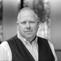 Professional portrait of a person in business attire with a dark vest and white shirt, black and white photo.