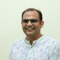 Person wearing glasses and a white and blue floral patterned shirt, smiling against a plain background.